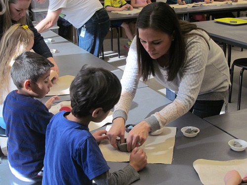 A volunteer Art Docent helps students make clay bird nests.